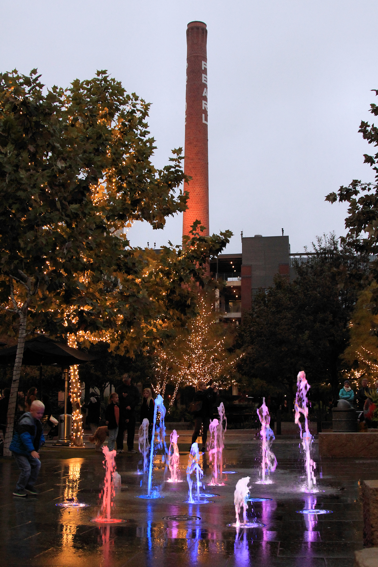 Children splashing in the fountains beneath the PEARL smokestack at dusk
